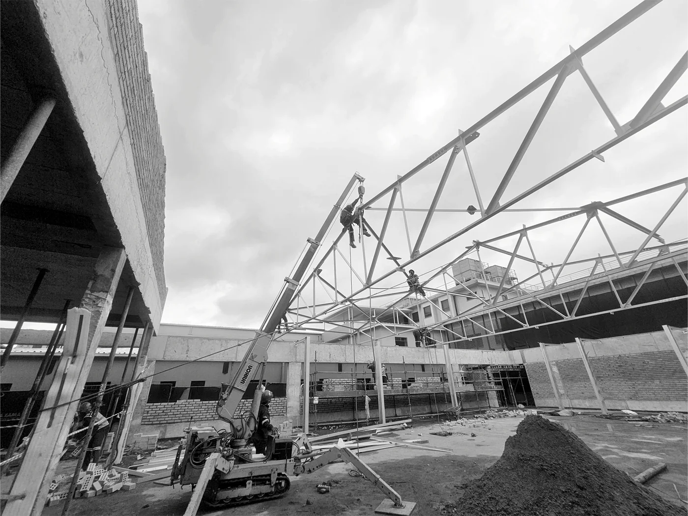 Structural-steel framing being assembled beside existing concrete construction